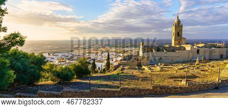Sunset Panoramic View Of The Pretty Village Of White Houses And Medieval Church Of Medina Sidonia In