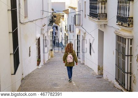Woman On Her Back Walking Through A Typical Andalusian Village Of White Houses And Metal Bars On The