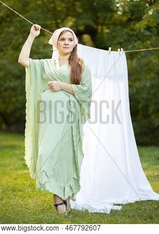 Pretty Pregnant Woman With Big Belly Stands Near Clothesline With Bed Sheet, Young Girl Takes Care O