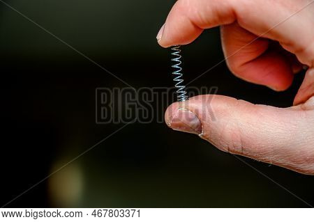 Caucasian Hand Compressing A Metal Spring Between A Thumb And Finger