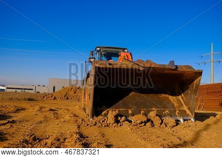 Tractor With Bucket In Sand And Clay.excavator At Construction Site On Houses And Blue Sky Backgroun