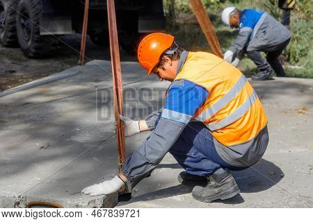 Slinger Lays Concrete Slab On Construction Site On Summer Day. Worker In Protective Vest And Constru