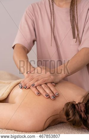 Female Masseur Massages The Back And Shoulder Blades Of A Young Brown-haired Woman In A Spa With Sof