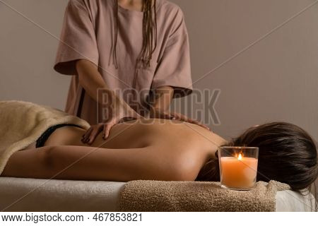 Female Masseur Does A Relaxing Back Massage In A Spa Salon With Lit Candles. Concept Of Health, Body