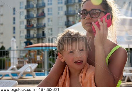 Resting After Swimming In Pool, Mother Talks On Phone, Hugs Boy, Wrapped In Towel. Mother And Son Si