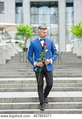 Elegant Man In Tux. Man Wearing Tux Bowtie Outdoor. Caucasian Tux Man With Red Rose