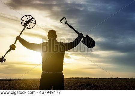 A Happy Treasure Hunter With A Metal Detector On The Background Of A Beautiful Sunset