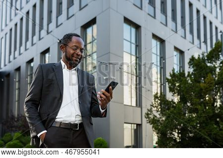 Successful And Satisfied African American Businessman Using Phone Outside Modern Office Building, Ma