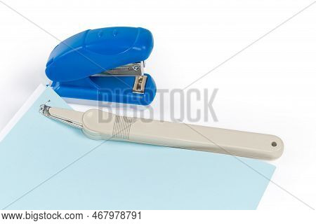 Simple Pen Type Staple Remover On The Stapled Blue And White Sheets Against The Small Manual Paper S