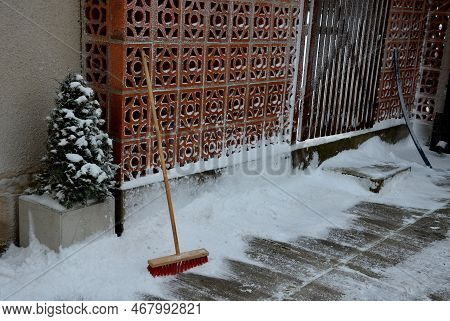 Cleaning The Yard From Snow To A Heavy Snowstorm. The Broom Rests Against A Perforated Brick Wall. C