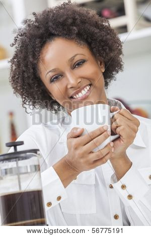 Una ragazza afro-americana bella felice di razza mista o una giovane donna bere caffè caffettiera in suo k