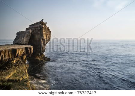 Beautiful Rocky Cliff Landscape With Sunset Over Ocean With Undientified People On Cliff Top