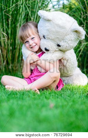 Little Cute Girl Sittinging In The Grass With Large Teddy Bear
