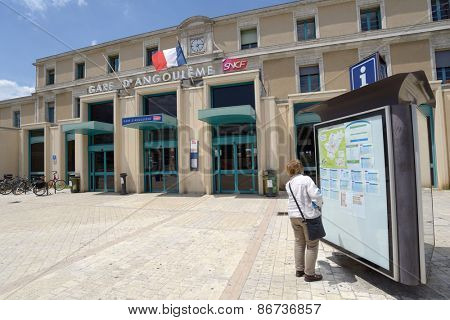 ANGOULEME, FRANCE - JUNE 26, 2013: Woman looking at timetables in front of train station. The station building is part of the former College Royal de la Marine