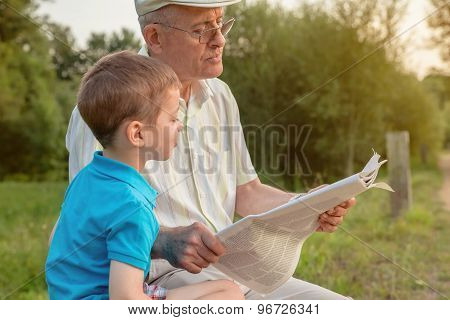 Senior man and child reading a newspaper outdoors