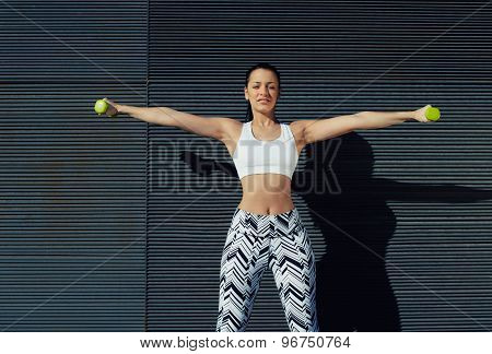 Smiling beautiful female exercising or working on her arms at outdoors while looking to you