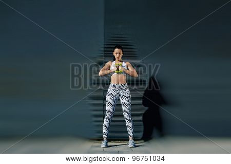 Beautiful female in workout gear holding weights with her hands together while training outdoors