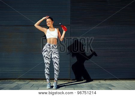 Happy female runner hold water bottle while standing against black wall background outdoors