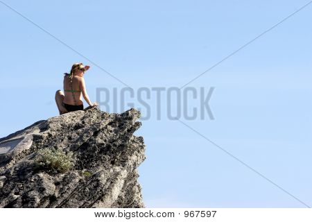 Mulher sentada sobre uma grande pedra perto do Oceano