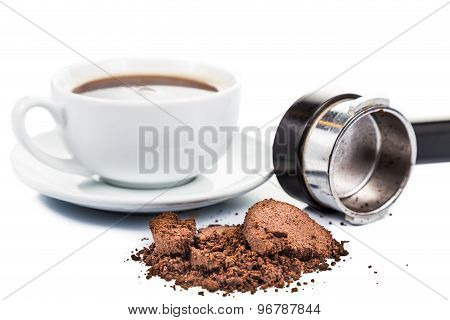 Spent or used coffee grounds with portafilter and a cup of freshly brewed coffee in the background