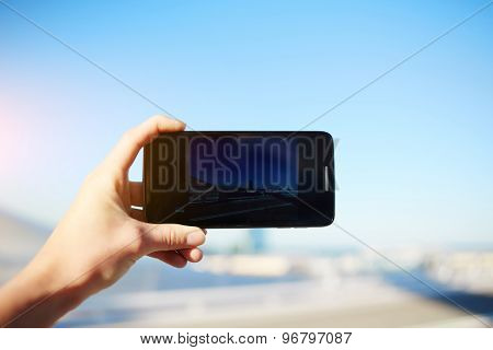 Tourist hand holding cell phone while taking a photograph of landscape in travel