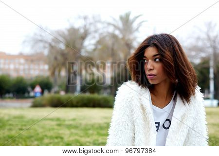 Young trendy female hipster in stylish clothing pensive looking away while sitting in the park