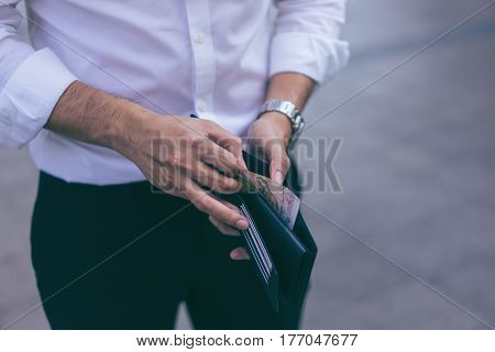 Man standing holding black wallet and picking up a money