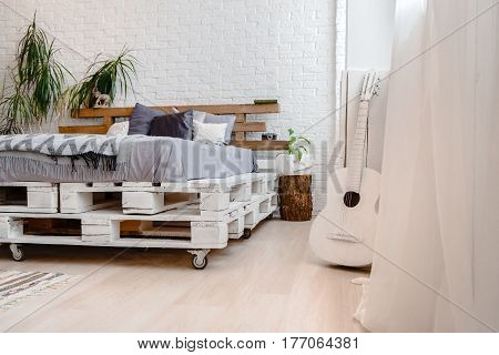 Daylight interior with bed, pallets and guitar