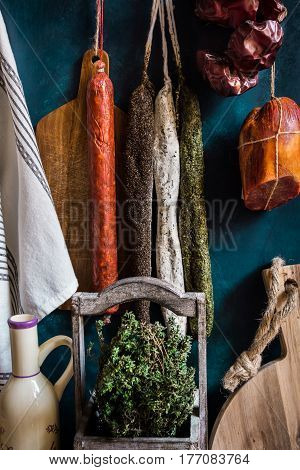 Variety of charcuterie sausages hanging on twine on hooks wood cutting bard herbs linen towel kitchenware pantry style rustic