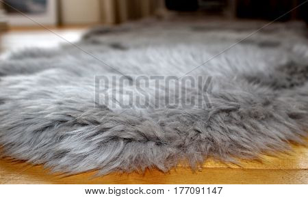 Close-up of fluffy grey faux fur floor rug on a wooden floor of young woman's house