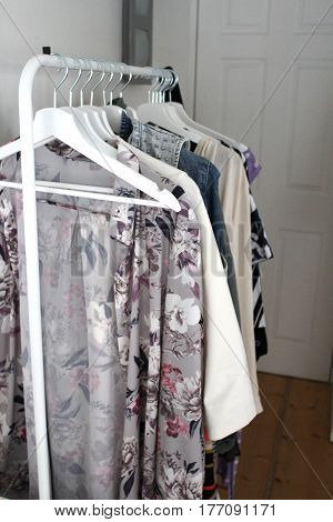 Contemporary white metal rack of clothes in modern flat with white hangers and wooden floor in dressing room / area