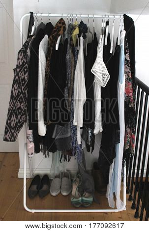 Contemporary white metal rack of clothes in modern flat with white hangers and wooden floor in dressing room / area
