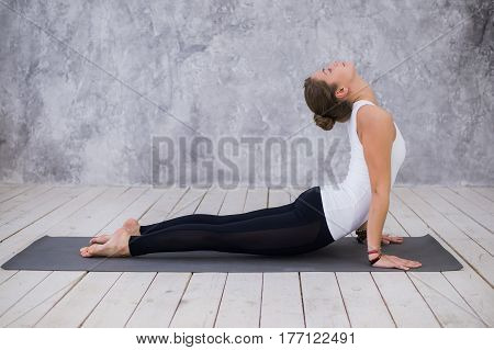 Beautiful young woman working out indoors, doing yoga exercise in the room with white walls, downward facing dog pose, adho mukha svanasana sun salutation pose, full length, side view.