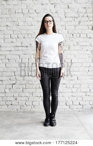 Young tattooed woman wearing blank t-shirt standing in front of brick wall in loft