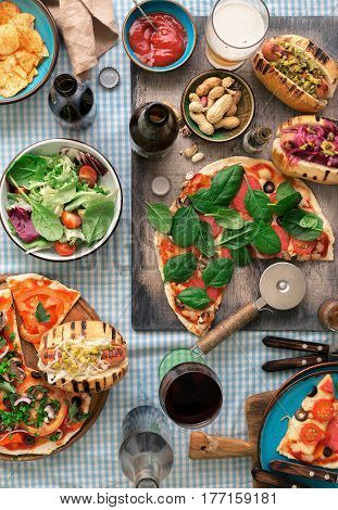 Outdoors food concept. Homemade pizza hot dogs wine beer and a snack for beer on the table top view