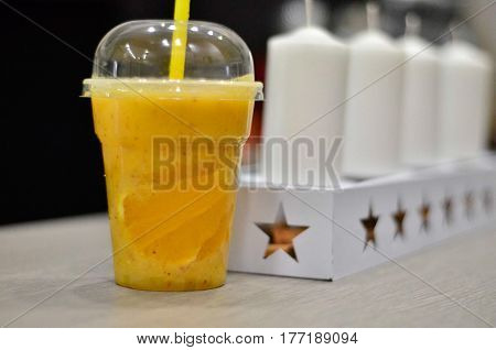 Natural orange juice in a plastic cup with straw, white tealight candles