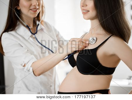 Female Medicine Doctor Holding Stethoscope To Pregnant Woman Standing For Encouragement, Empathy, Ch
