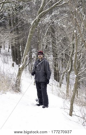 Rugged outdoorsman hiking through snow covered forest looking for fishing winter scene