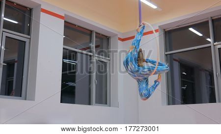 Plastic beautiful girl gymnast on acrobatic circus ring in blue suit. Aerial ring. Acrobatic and sport concept