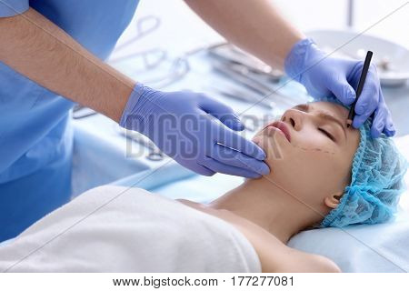 Plastic surgeon drawing marks on female face in clinic