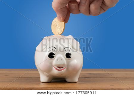 Pottery piggy bank on a table or shelf with a hand inserting a gold coin for savings or investment in the future