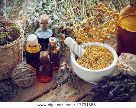 Tincture bottles mortar of dried marigold flowers and healing herbs on wooden board. Herbal medicine.