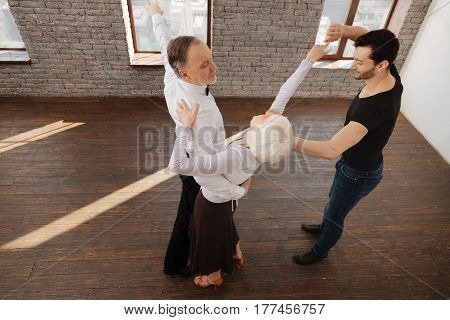 Teaching gracefulness. Careful skilled charming dance couch teaching aged pensioners tango while having training session and expressing care