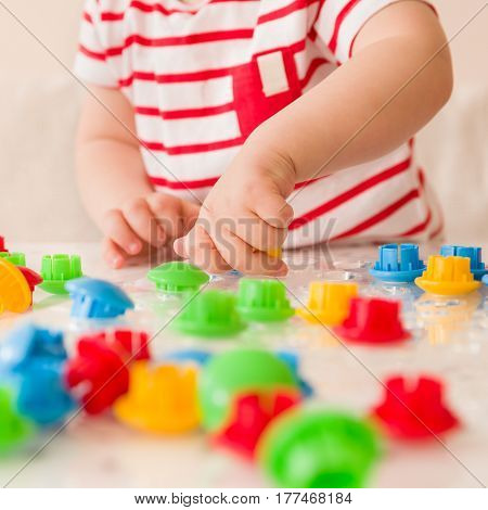 Closeup of child's hand taking bright mosaic parts. Playing and learning colors at home. Toddler boy in a striped shirt playing with colorful constructor details. Activities with children