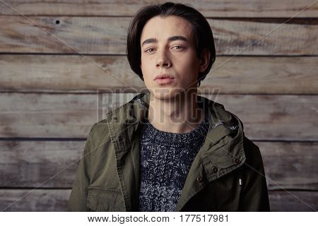 Handsome man wearing green jaket and torn jeans in wooden rural house interior