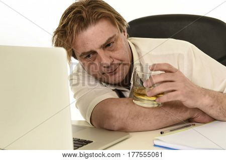 wasted and messy alcoholic businessman drinking whiskey working at laptop computer desk at office looking drunk and hangover in alcoholism problem and alcohol abuse concept