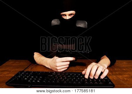 Dangerous hacker in balaclava holding gun