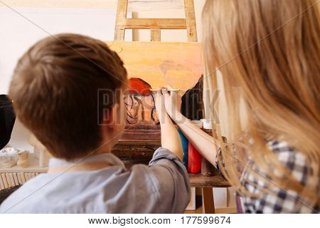 Our weird masterpiece. Skilled young helpful kids sitting in the art studio and having painting class while painting in the interaction with each other