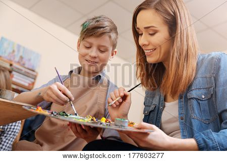 My lovely working hours . Smiling involved skillful painter sitting in the studio and conducting art class while teaching child painting