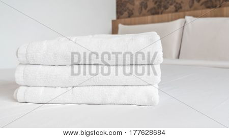 Three white laundered fluffy towels on white bed in bedroom interior at the hotel